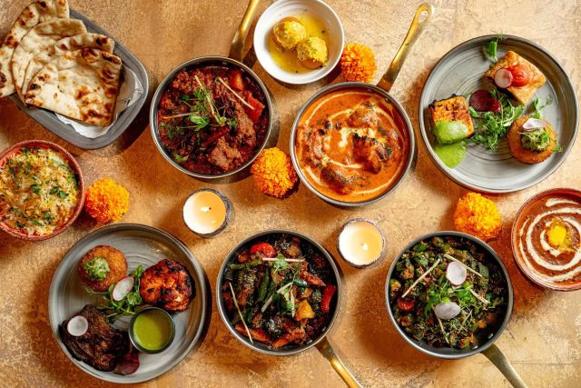 Festive Diwali feast featuring various Indian curries, naan, and starters decorated with lit candles at Riwaz restaurant in Beaconsfield